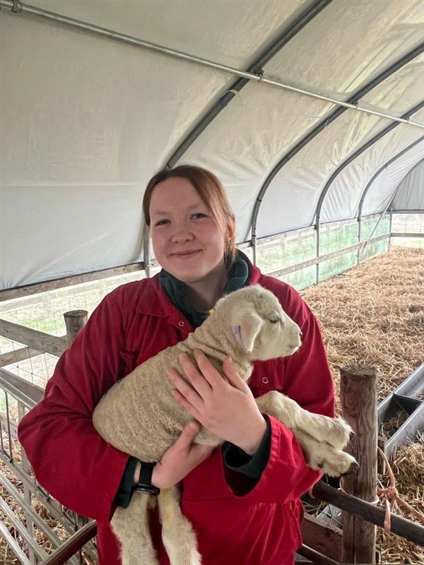 Student Recruitment and Events Officer Sophie Holbourne smiling while holding a lamb at the college